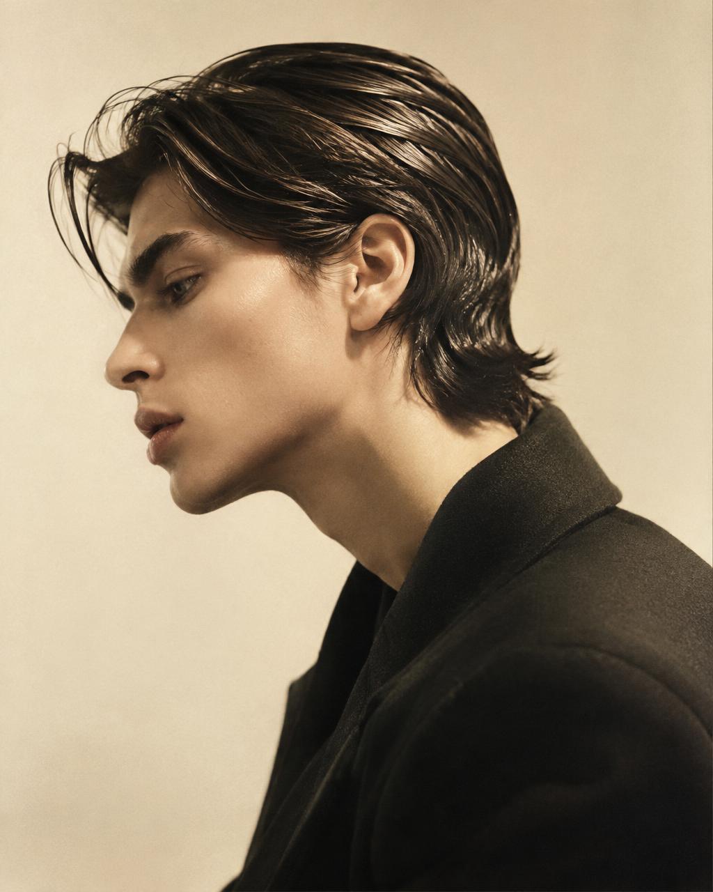 Editorial portrait: model in profile with sleek, swept-back dark hair against a warm ivory backdrop